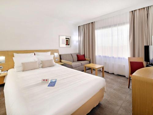 um quarto de hotel com uma grande cama branca e um sofá em Novotel Katowice Centrum em Katowice