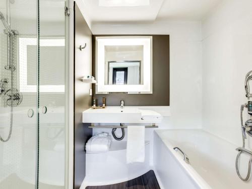 a bathroom with a sink and a tub and a mirror at Novotel Suites Paris Stade de France in Saint-Denis