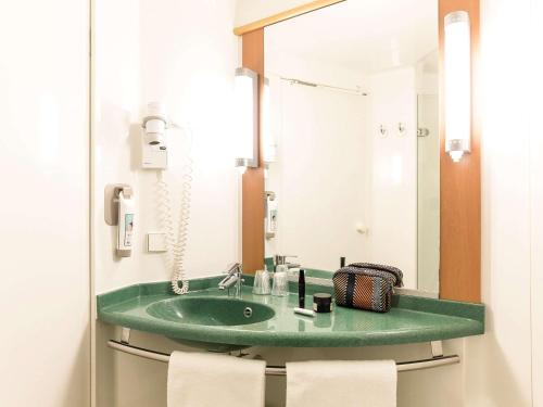 La salle de bains est pourvue d'un lavabo vert et d'un miroir. dans l'établissement Ibis Valencia Bonaire Aeropuerto, à Aldaya