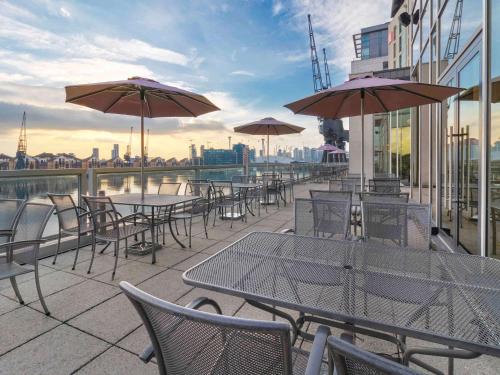 a group of tables and chairs with umbrellas on a building at Novotel London Excel in London
