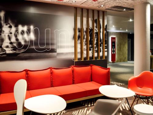a red couch in a lobby with white tables and chairs at ibis Honfleur in Honfleur
