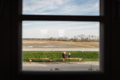 two people sitting on a bench looking out a window at Haus Anna Elbe, Bauernhaus-Ferienwohnungen an der Elbe in Hamburg