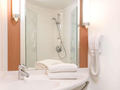 een badkamer met een douche en een wastafel met handdoeken bij ibis Vitré Centre in Vitré