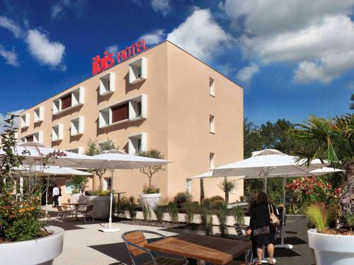 a woman standing in front of a hotel with tables and umbrellas at ibis Loriol Le Pouzin in Le Pouzin