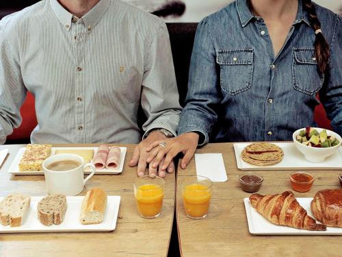 two people sitting at a table with food and drinks at ibis Issy les Moulineaux "Val de Seine" in Issy-les-Moulineaux