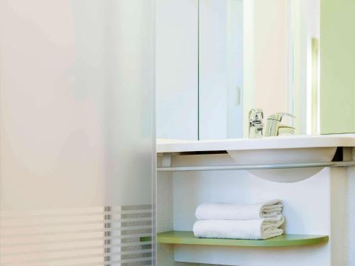 ein Badezimmer mit einem Waschbecken, einem Spiegel und Handtüchern in der Unterkunft ibis Budget Brussels South Ruisbroek in Ruisbroek
