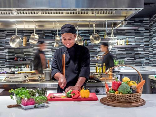 a chef cutting vegetables on a cutting board in a kitchen at Novotel Bangkok IMPACT in Nonthaburi