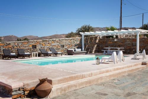 a swimming pool with chairs and a stone wall at Kea Villa Thea- Villa Ilios in Vourkarion
