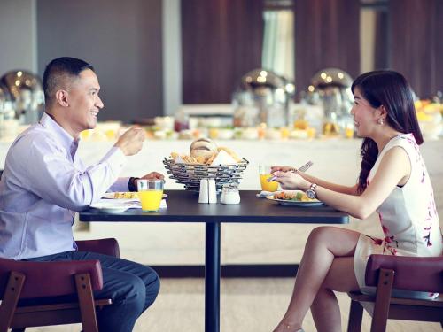 a man and woman sitting at a table eating food at Mercure Karawang in Karawang