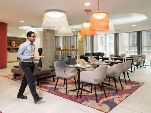 a man walking through a restaurant with a table and chairs at Aparthotel Adagio Birmingham City Centre in Birmingham