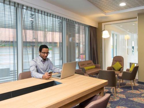 a man sitting at a table with a laptop at Aparthotel Adagio Birmingham City Centre in Birmingham