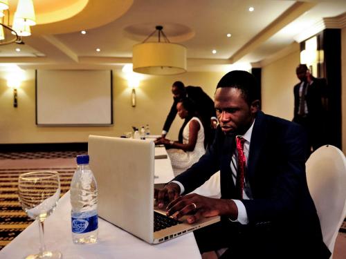 a man sitting at a table using a laptop computer at Pullman Lubumbashi Grand Karavia. in Lubumbashi