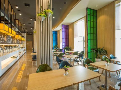 a restaurant with wooden tables and green chairs at ibis Styles Changsha Intl Exhibition Ctr in Huangxing