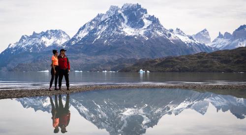 two people standing next to a body of water with a mountain at Río Serrano Hotel + Spa in Torres del Paine