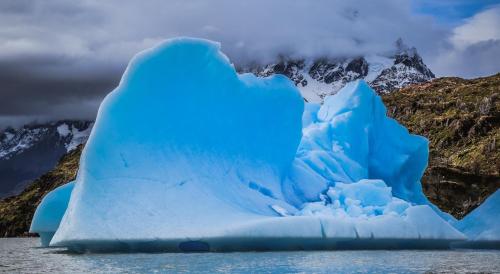 an iceberg in the water with mountains in the background at Río Serrano Hotel + Spa in Torres del Paine