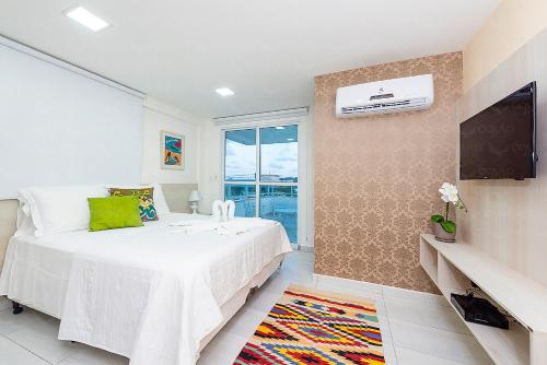a bedroom with a white bed and a tv at Águia Flats Pousada in Natal