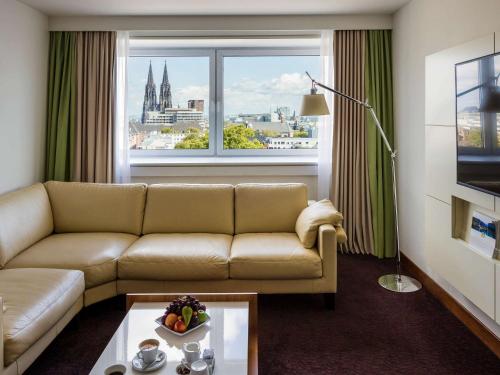 a living room with a couch and a large window at Pullman Cologne in Cologne