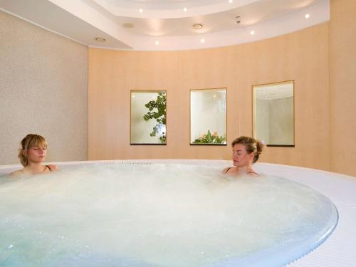 two women sitting in a bath tub in a bathroom at Novotel Hannover in Hannover