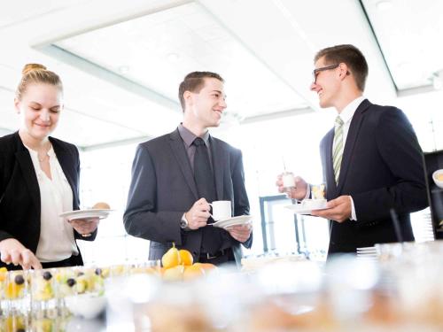 a group of people standing around a table with plates of food at Novotel Hildesheim in Hildesheim