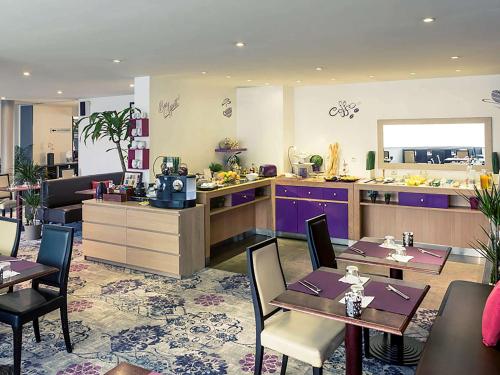 a restaurant with tables and a kitchen with purple cabinets at Hotel Mercure Rennes Cesson in Cesson-Sévigné