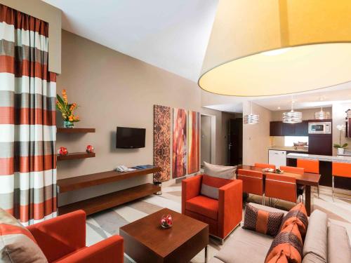 a living room with orange furniture and a kitchen at Novotel Dubai Al Barsha in Dubai