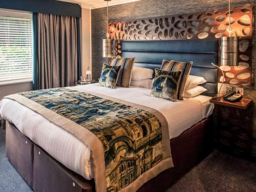 a bedroom with a large bed with a blue headboard at WorldHotels Distinctive Woughton House Hotel in Milton Keynes