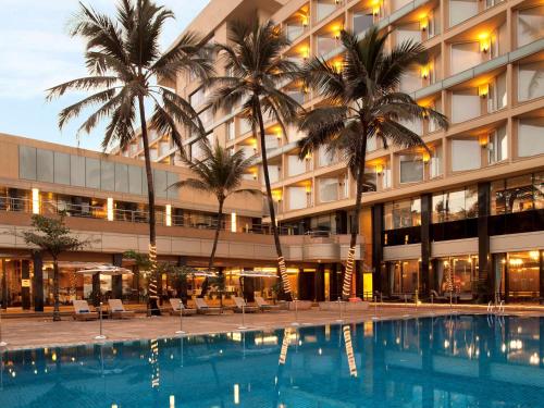 un hôtel avec une piscine en face d'un bâtiment dans l'établissement Novotel Mumbai Juhu Beach, à Mumbai