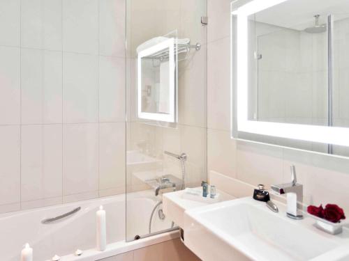 a white bathroom with a sink and a tub and a mirror at Novotel Abu Dhabi Gate in Abu Dhabi