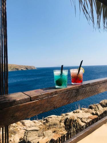 three glasses sitting on top of a wooden rail overlooking the ocean at Hersonissos Andros in Gavrion