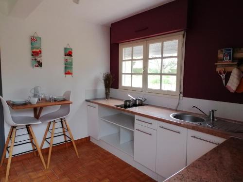 une cuisine avec des armoires blanches, un évier et une fenêtre dans l'établissement Proche mer, cadre verdoyant avec parking, à Clohars-Carnoët