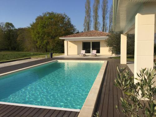 a swimming pool with a wooden deck and a house at Chambre d'hôtes Ama in Pompignac