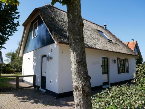 a cottage with a thatched roof and a tree at Buitenplaats Villa Deluxe in Callantsoog