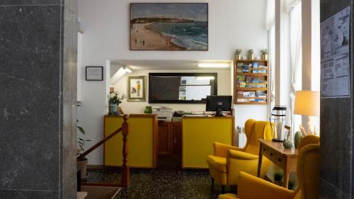 uma sala de espera com cadeiras amarelas e uma secretária em Hotel Josein em Comillas