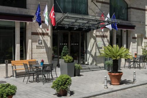 イスタンブールにあるHoliday Inn Istanbul Old City, an IHG Hotelの建物の前にテーブルと椅子、旗が並ぶパティオ