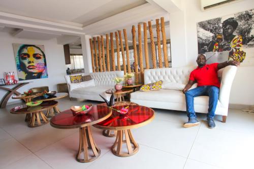 a man sitting on a couch in a living room with tables at The Swiss Hotel Freetown in Freetown