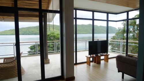 a living room with a television and large windows at La Estancia Busuanga in Busuanga