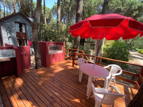 a wooden deck with a table and chairs and a red umbrella at Complejo de Cabañas Tunquelen in Mar de las Pampas