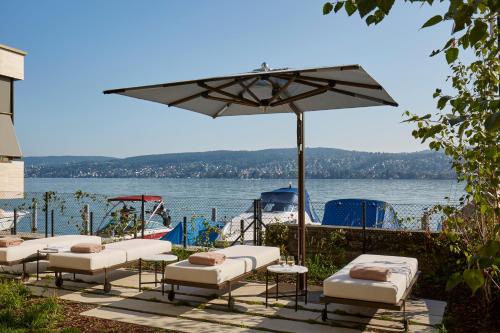a group of chairs and an umbrella next to the water at Alex Lake Zürich in Thalwil