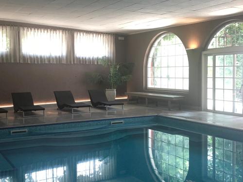 una piscina con sillas, una mesa y ventanas en Hotel Vecchia Stazione Mountain Elegance, en Roana