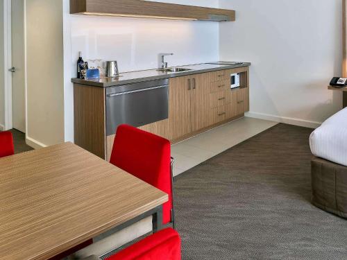 a kitchen with a sink and a table with red chairs at Novotel Sydney West HQ in Rooty Hill