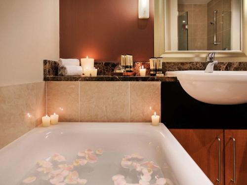 a bathroom with a tub with candles and a sink at The Sebel Auckland Viaduct Harbour in Auckland