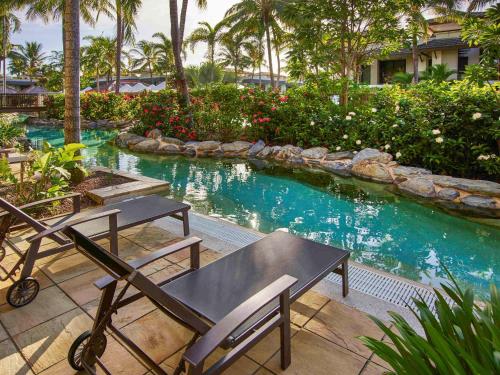 a pool with two chairs and a table in a yard at Pullman Port Douglas Sea Temple Resort and Spa in Port Douglas