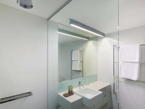 a white bathroom with a sink and a mirror at East Perth Suites Hotel in Perth