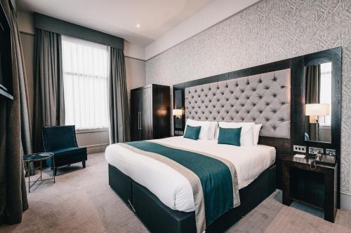 um quarto de hotel com uma cama grande e uma cadeira em The Station Hotel em Aberdeen