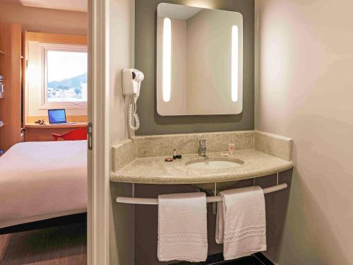 a bathroom with a sink with a mirror and a bed at ibis Jundiai Shopping in Jundiaí