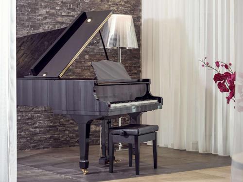 a black piano with a chair and a lamp at Mercure Hotel Golf Cap d'Agde in Cap d'Agde