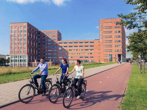 three people riding bikes down a road in a city at Mercure Amsterdam Sloterdijk Station in Amsterdam