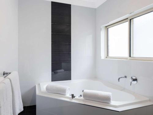 Mercure Goulburn في غولبورن: حمام أبيض مع حوض استحمام ونافذة