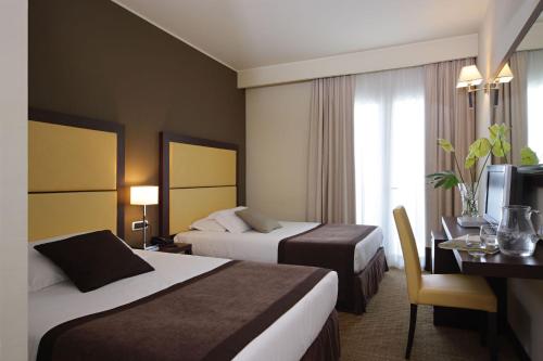 a hotel room with two beds and a desk at Hotel Aqua in Abano Terme