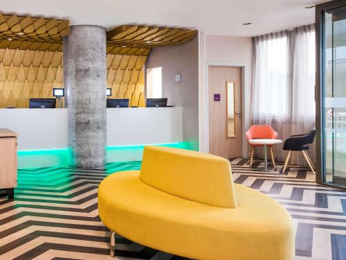 a yellow chair in a lobby with a reception desk at ibis Styles London Heathrow Airport in Hillingdon